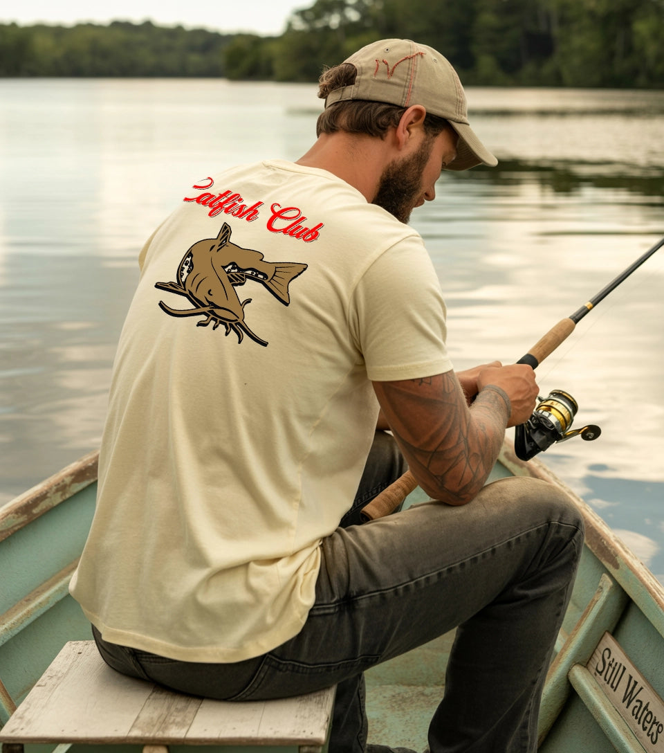 Man fishing from a boat wearing Tee Nation’s Catfish Club Natural Comfort Colors T-shirt – perfect for catfish lovers and outdoor enthusiasts.