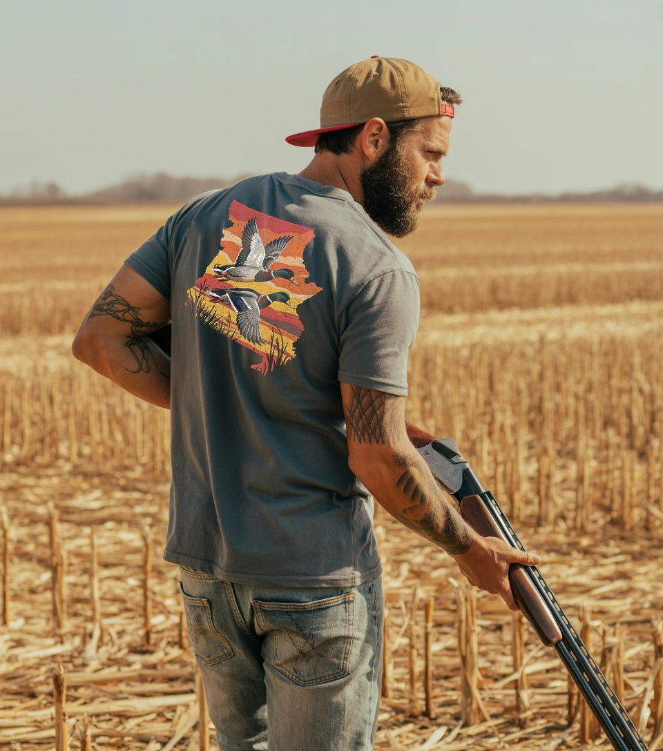 A man duck hunting in a corn field wearing a grey comfort colors Missouri Duck Hunting t-shirt.